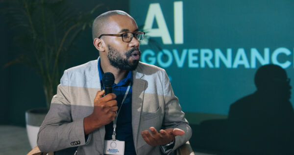 Ein Mann hält ein Mikrofon in der Hand, er scheint eine lebhafte Diskussion zu führen. Im Hintergrund ist der Titel einer Veranstaltung zu sehen: AI Governance.