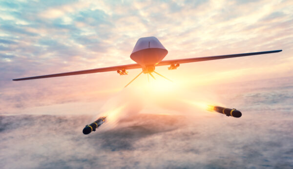 Eine militärische Drohne UAV fliegt vor einem wolkigen Himmel und feuert zwei Geschosse ab.